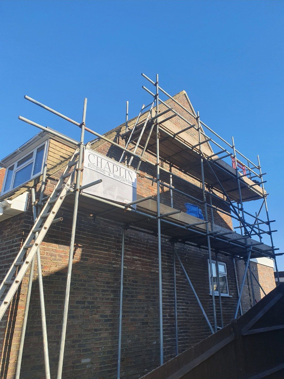 House under scaffold with a CHAPLIN banner, blue sky behind